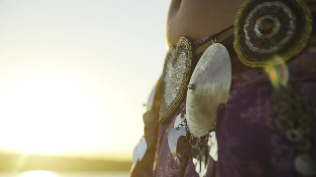 Girl dancing belly dance close-up with iron decorations on a skirt in summer at sunset