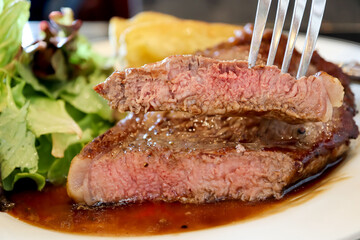 Close-up piece sliced in the fork of sirloin beef steak with brown sauce in white plate background. Medium level ripe. Foods concept.