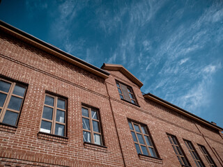 Fototapeta na wymiar A brown old brick building with brown plastic windows in the foreground. Blue sky and some clouds in the background. An old building after restoration.
