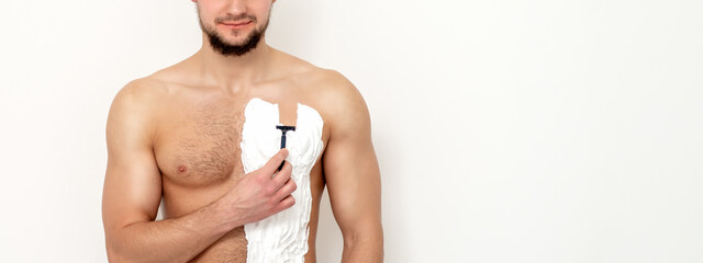 Young caucasian man with beard holds razor shaves his chest with white shaving foam on white background. Man shaving his torso