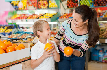 Fototapeta premium Portrait of happy cheerful smiling woman and her little son choosing oranges at shop