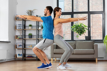 Fototapeta premium sport, fitness, lifestyle and people concept - smiling man and woman exercising and doing squats at home