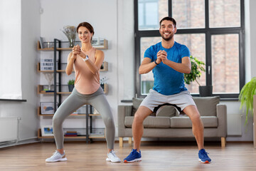 Fototapeta na wymiar sport, fitness, lifestyle and people concept - smiling man and woman exercising and doing squats at home