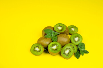 several kiwis, whole and cut, on a yellow background with mint leaves