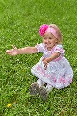 Little girl in beautiful dress sits on the grass and stretches her arms forward