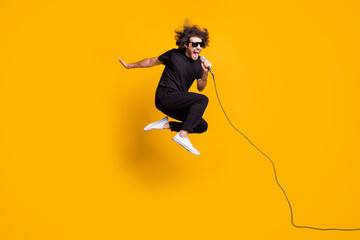 Full length body size portrait of jumping man wearing black clothes singing loudly in microphone...