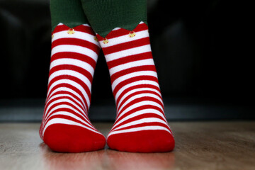 Female legs in Christmas socks on the wooden floor. Concept of New Year celebration, elf costume