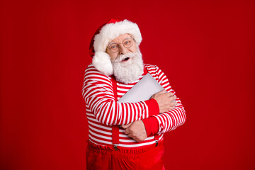 Portrait of his he nice handsome cheerful cheery bearded Santa father holding in hands hugging laptop North Pole December wintertime isolated bright vivid shine vibrant red color background
