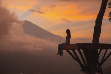 Silhouette of a girl in a long dress sitting near Bali landmark volcano Agung view. Travel blogger,...