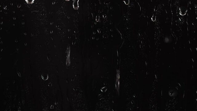 Rain drops falling down on window over black background, raining at night, 4K