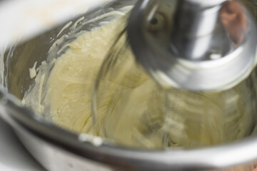 Close up creaming cream cheese to soften in the food mixer machine bowl for making cheesecake or other bakery products.