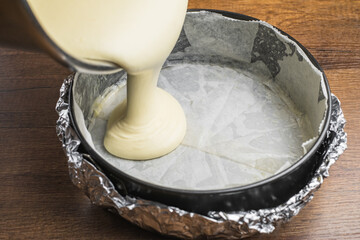 Pouring cake mixture into a cake tin line with paper and wrap with aluminum foil for baking cheesecake.