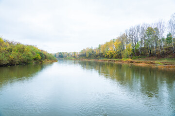 Calm river with trees on the shores in rainy autumn day. Autumn landscape. 