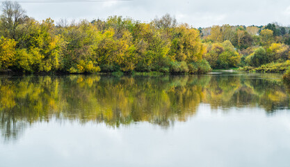 Fototapeta na wymiar Calm river with trees on the shores in rainy autumn day. Autumn landscape. 
