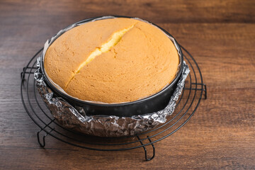Freshly baked fluffy japanese cheesecake in cake tin on a cooling rack on wood table top.