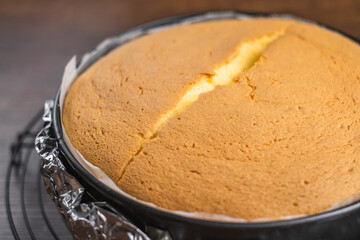 Close up freshly baked fluffy japanese cheesecake in cake tin on a cooling rack on wood table top.
