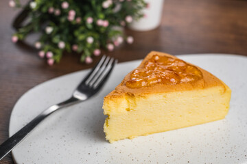 A piece of fluffy soft Japanese style cheesecake with orange jam on top on a white stone plate on wood tabletop.