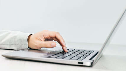 Side view of slim silver laptop on a grey desk. Female hand using the keyboard of laptop. Copy space. Minimal. Office or remote work, banking or shopping