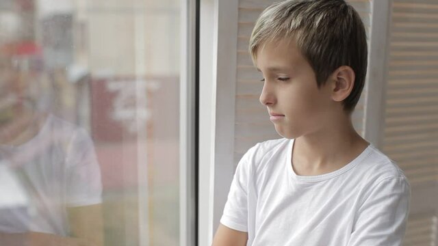 Boy sitting near the window and looking to the street