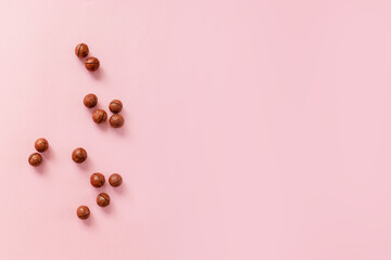 Raw macadamia nut scattered on a pink solid background with copy space. Minimal composition.