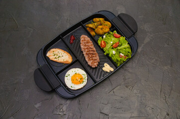 Breakfast, fried steak or cutlet, salad with tomato and green vegetables, croutons, potatoes, egg , view from the top, dark background. Concept healthy eating, diet, menu, nutritious food.