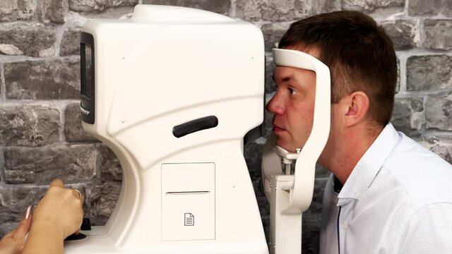 Portrait of man during test on refractometer machine, side view. Eye exam for man at optical store.