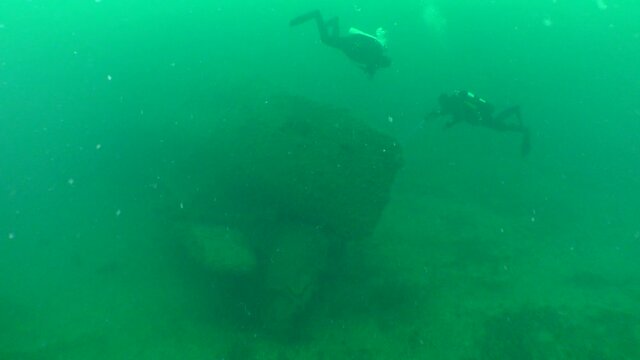 Two divers near the stern of a sunken submarine.