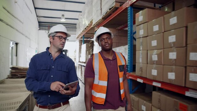 Manager inspecting parcels holding digital tablet while worker shows order of packages in factory warehouse