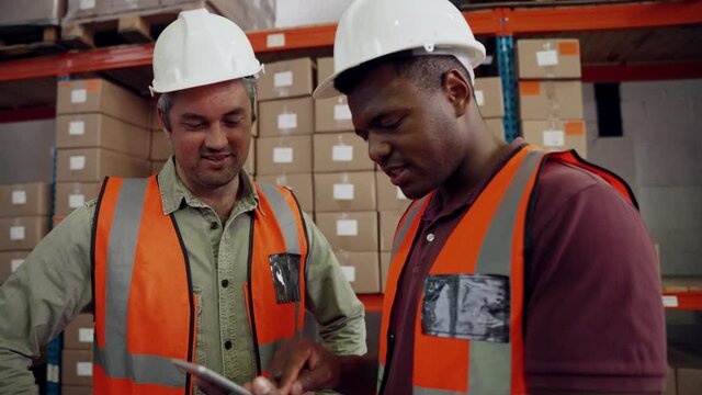 Male colleagues discussing business emails on digital tablet standing in factory warehouse 