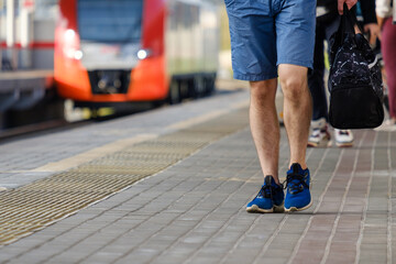 Legs of a man in shorts and sneakers walking along the platform of a railway station against the...