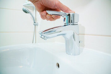 Man is  closing water flow tap  with water. Water running from chrome faucet.