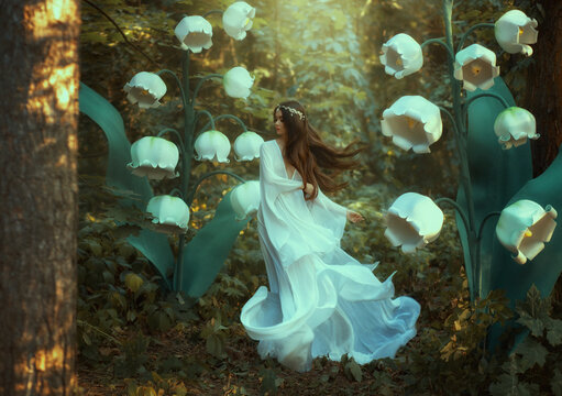 A beautiful girl elf walks in a fantasy forest. Huge flowers lilies of the valley, green trees, creative decorations. White long dress and hair flying in wind in motion. Woman with a silver diadem