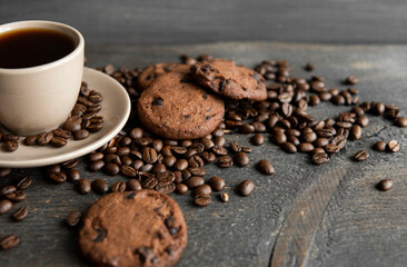 Coffee cup with cookies on wooden table background. Mug of black coffee with scattered coffee beans and cookies on a wooden table. Fresh coffee beans.