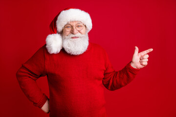 Photo of old man retired pensioner in santa haus headwear point index finger copyspace demonstrate holly jolly x-mas adverts promotion wear bright sweater isolated shine color background