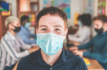 Portrait of worker wearing face protective mask during coronavirus outbreak - Caucasian man inside coworking office - Social distance and job healthcare concept