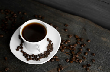 Coffee cup with roasted coffee beans on wooden table background. Mug of black coffe with scattered...