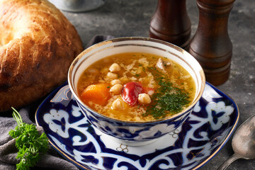 Traditional asian shurpa soup in traditional ornament bowl on ray background