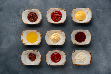 Different tasty sauces in bowls, various sauces on gray stone background, top view
