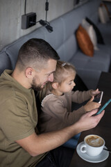 Father with little girl spend time in cafe, addicted to theirs smartphones. Man and child playing playing with phone in cafe.