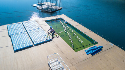 Aerial view of a girl riding a bicycle across a lake on a tightrope