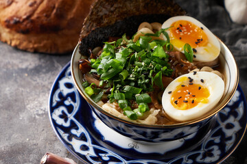 Traditional asian ramen noodle soup with chicken and eggs on gray background