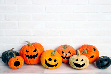 Halloween pumpkin head Jack lantern with funny faces on the table against a white brick wall background.