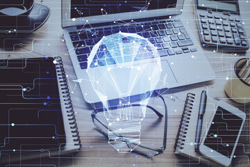 Computer on desktop in office with bulb icon hologram. Double exposure. Concept of idea.