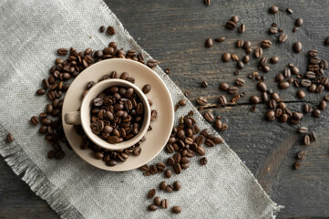 Coffee cup filled of fresh arabica or robusta coffee beans with scattered coffee beans on a linen textile and wood table.