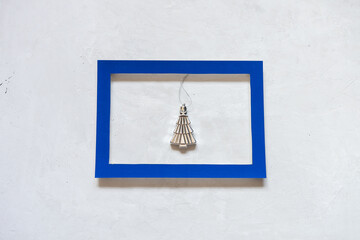 Small silver Christmas tree in a blue frame on a gray concrete background.