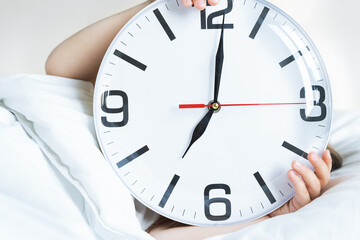 Little sleeping girl with big, huge clock in hands. Early morning wake up before kindergaten,school. White pillow, blanket in bed. Sleepy child. Sweet dreams. Bedtime. Correct mode of children's rest