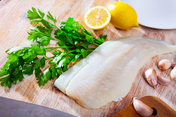 Fresh cod fillet with parsley and lemon on wooden board