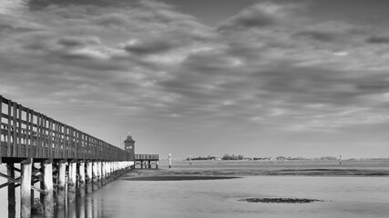 Wooden pier and lighthouse on the Adriatic sea, Lignano Sabbiadoro, Italy. Black and white landscape.