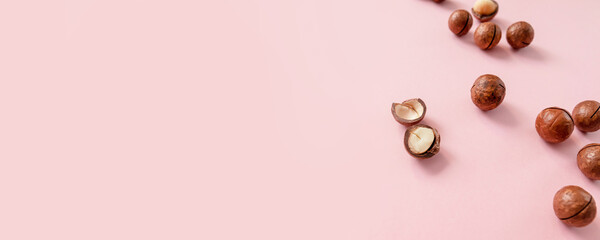 Cracked macadamia nuts on pink background with copy space