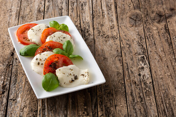 Traditional caprese salad with tomato and mozzarella cheese on rustic wooden table.	Copy space